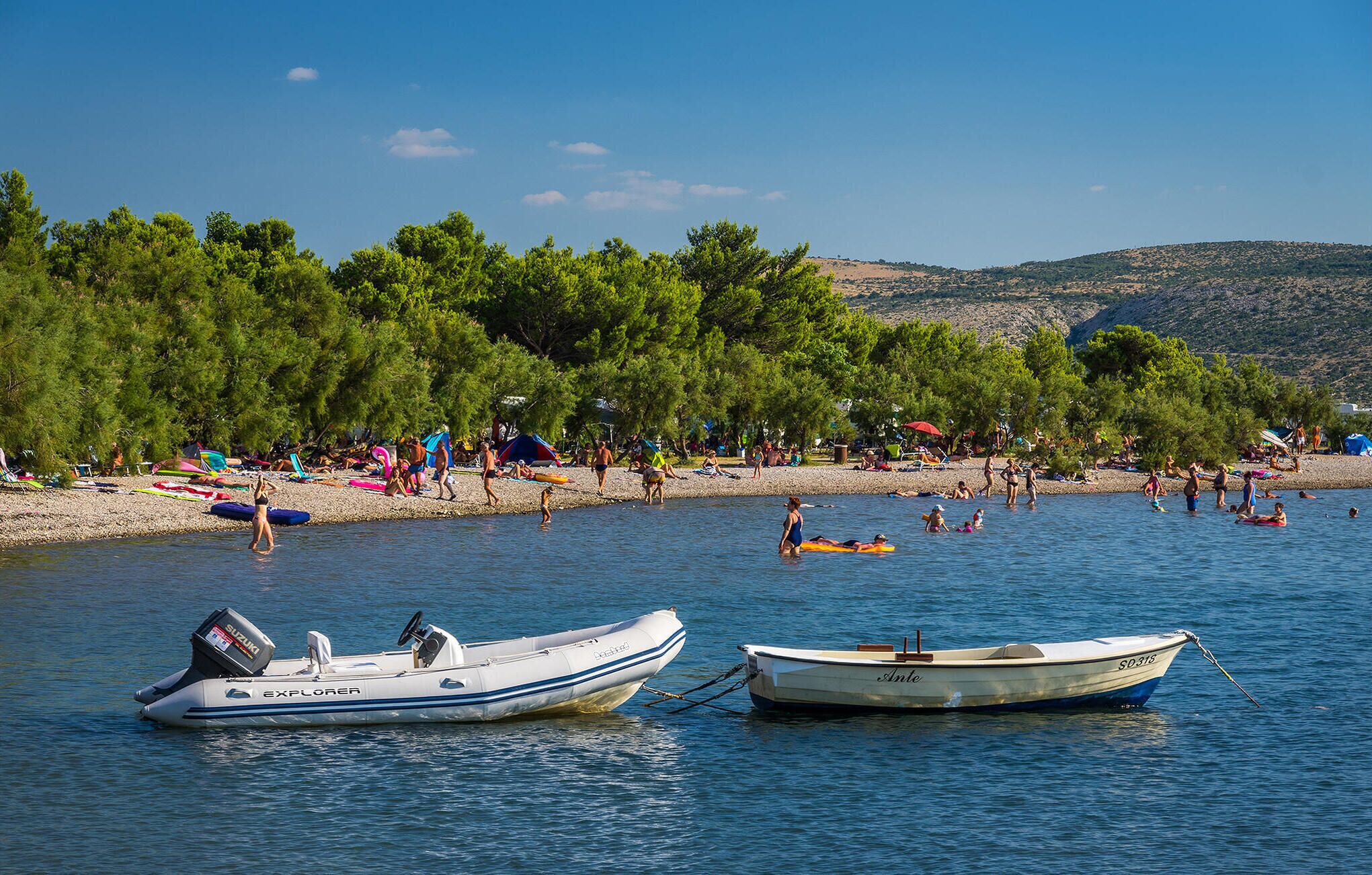 A beach with boats anchored in the water, a sandy shore, and trees in the background.