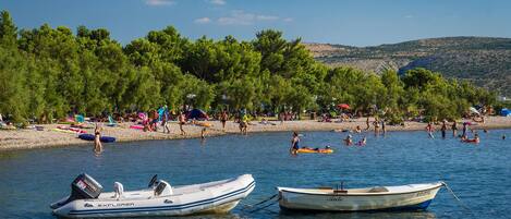 A beach with boats anchored in the water, a sandy shore, and trees in the background.