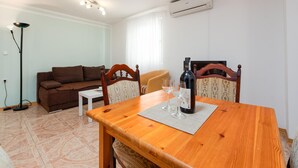 A dining area with a wooden table, two chairs, a wine bottle, and glasses. There is a brown sofa and a white table in the background. - 1 bedroom awesome apartment in Seline (Seline)
