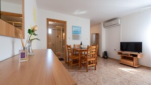 A modern living room with a wooden dining table, chairs, a TV, and a large window. - Nice apartment in Seline with WiFi (Seline)