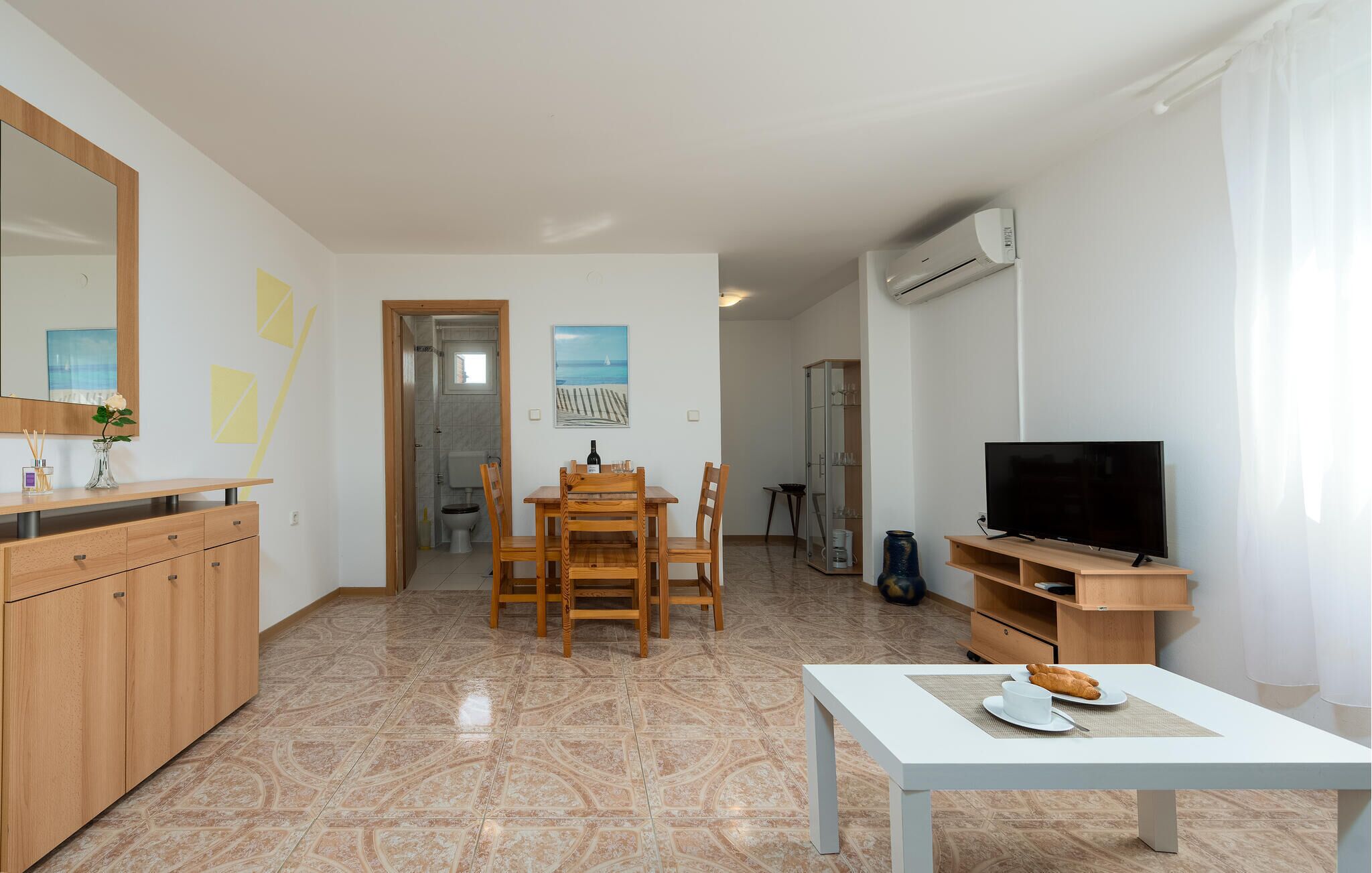 A modern living room with a dining area, a TV, and a kitchen.
