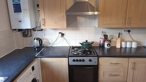 Una cocina con armarios de madera, estufa a gas, horno empotrado, lavadora y calentador de agua.