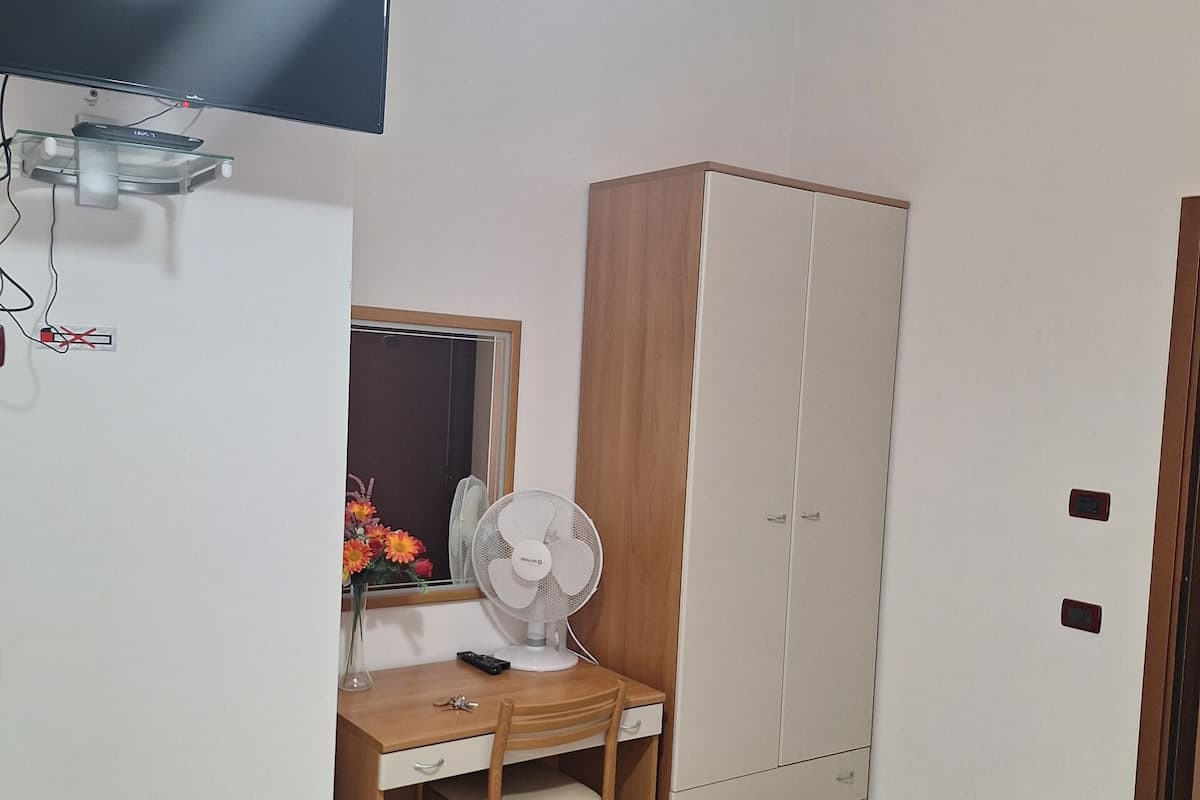 A room with a desk, chair, wardrobe, and a television mounted on the wall.