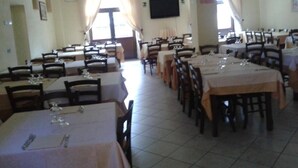 Un espace repas comprenant plusieurs tables et chaises, un téléviseur à écran plat fixé au mur et de grandes fenêtres dotées de rideaux.