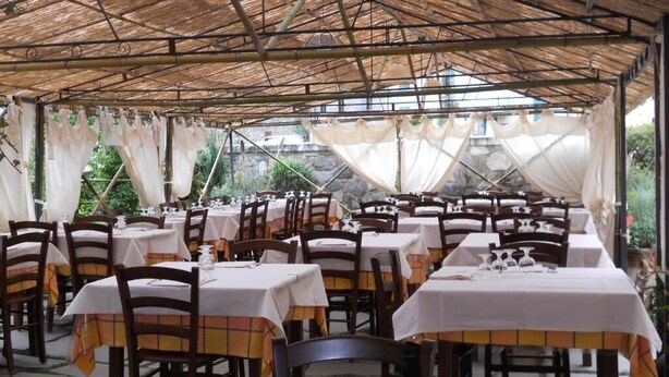 Un espace extérieur aménagé pour les repas, avec des tables et des chaises sous un toit en bambou.
