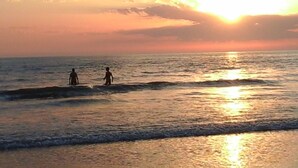 Un coucher de soleil sur l’océan, avec deux personnes debout dans l’eau.