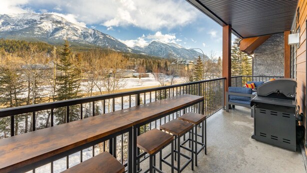 A balcony with a wooden table and benches, overlooking a snowy mountain landscape. - Designed Specifically for Large Families (Canmore)