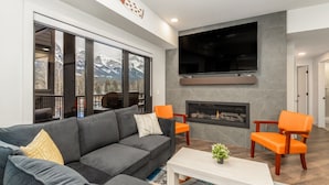 A modern living room with a grey sofa, orange chairs, a white coffee table, and a fireplace. - 1,250 SF Luxury Home | 4-BR + 3-BA & 8 Beds | Best Amenities in Canmore (Canmore)