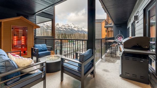 A balcony with a fire pit, seating, and a grill, overlooking a snowy mountain range. - 1,250 SF Luxury Home | 4-BR + 3-BA & 8 Beds | Best Amenities in Canmore (Canmore)