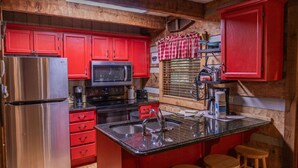 A compact kitchen with red cabinets, a stainless steel refrigerator, a microwave, and a sink with stools. - Cabin on the lake! Hot tub, fishing, pool access! (Sevierville)