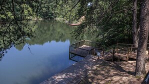 A wooden dock extending into a calm lake surrounded by dense trees. - Cabin on the lake! Hot tub, fishing, pool access! (Sevierville)