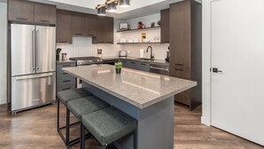 A modern kitchen with a large island, stainless steel appliances, and dark wood cabinetry. - Luxury 8-BR Family Home with Exceptional Amenities (Canmore)