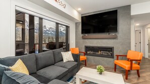 A modern living room with a grey sofa, orange chairs, a white coffee table, and a fireplace. - Luxury 8-BR Family Home with Exceptional Amenities (Canmore)