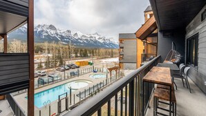 A balcony with a pool, outdoor seating, and a mountain view. - Luxury 8-BR Family Home with Exceptional Amenities (Canmore)
