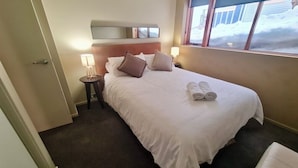 A hotel room with a large bed, two bedside lamps, a window with a view, and a small bedside table. - Absollut 9 - Central location (Mount Hotham)