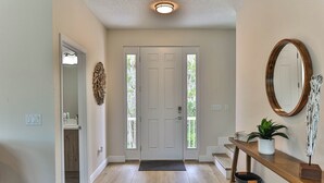 Un pasillo con una puerta blanca, una consola de madera con una planta y un espejo en la pared.