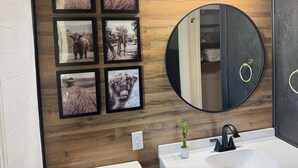 Ein Badezimmer mit Holzvertäfelung, einem runden Spiegel, einem weißen Waschbecken und sechs gerahmten Bildern.