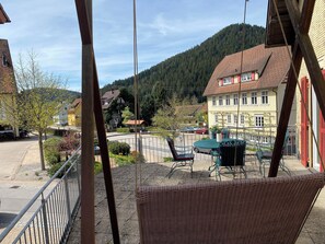 A balcony with wicker furniture, a view of a village street, and houses in the background. - Central and modern apartment close to the hiking trails (Baiersbronn)