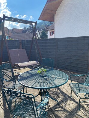 A patio with a swing set, a round metal table, and four chairs. - Central and modern apartment close to the hiking trails (Baiersbronn)