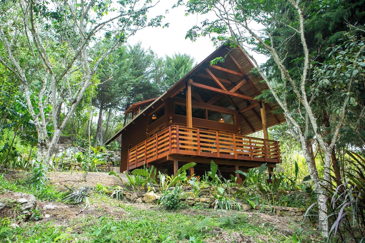 A wooden cabin with a balcony, surrounded by dense forest.