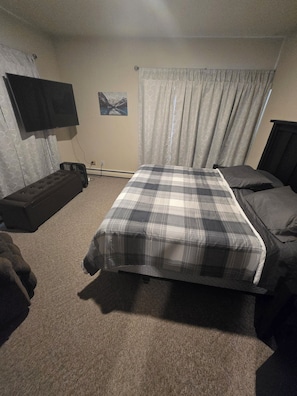 Un dormitorio con cama, una banca, televisor y un cuadro colgado en la pared.