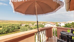 Un balcón con una sombrilla beige, una mesa con sillas y vistas a casas y vegetación.