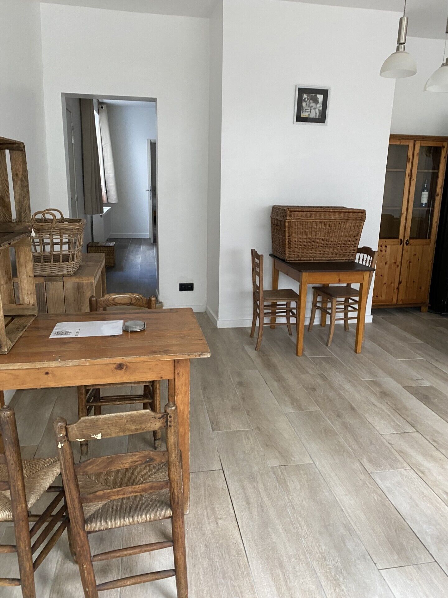 Un coin repas avec une table et des chaises en bois, un panier posé sur la table et une porte visible au fond.