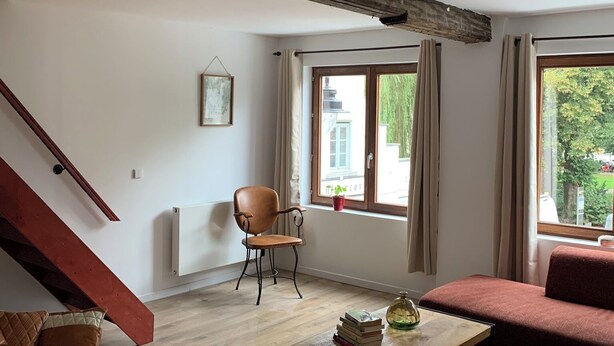 A spacious living room with a wooden staircase, a comfortable armchair, a sofa, and a coffee table. - Soothing 7-bedroom house with WiFi in Ronse. (Ronse)