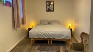 A bedroom with a bed, two bedside lamps, a chair, a rug, and a painting on the wall. - Soothing 7-bedroom house with WiFi in Ronse. (Ronse)