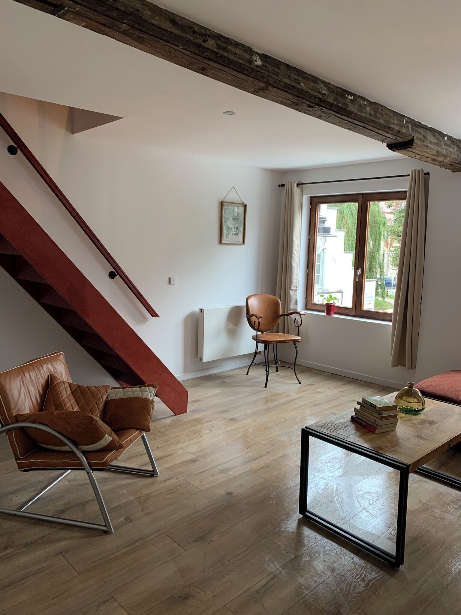 Amplia sala de estar con una escalera de madera, un sillón de cuero, una mesa de centro de madera y vistas a través de un gran ventanal.
