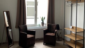A room with two brown armchairs, a wooden shelf unit, a radiator, a potted plant, and a window with curtains. - Soothing 7-bedroom house with WiFi in Ronse. (Ronse)