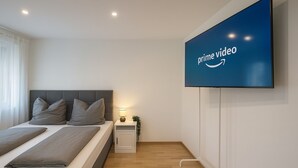 Une chambre à coucher moderne, avec un lit, une table de chevet, une lampe et un téléviseur fixé au mur.