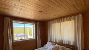 A wooden-paneled bedroom with a bed, curtains, and a window with a view.