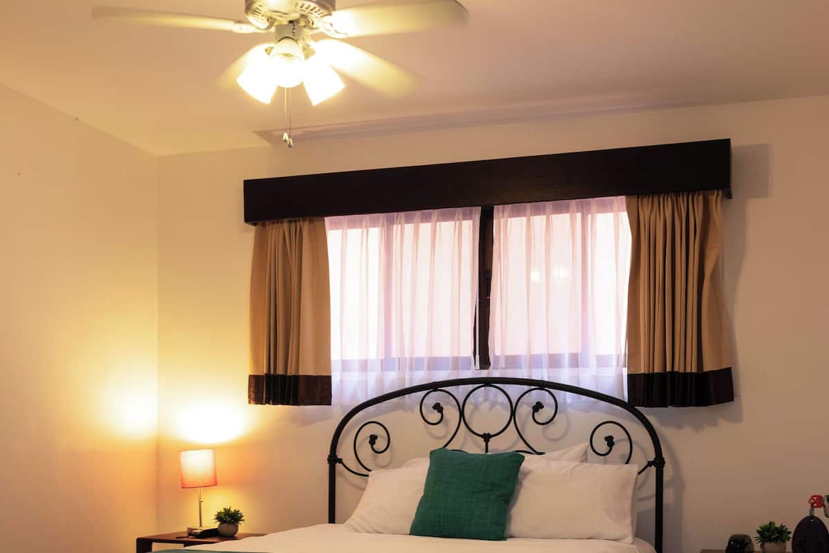 A neatly made bed with a green throw, a bedside lamp, and a ceiling fan.