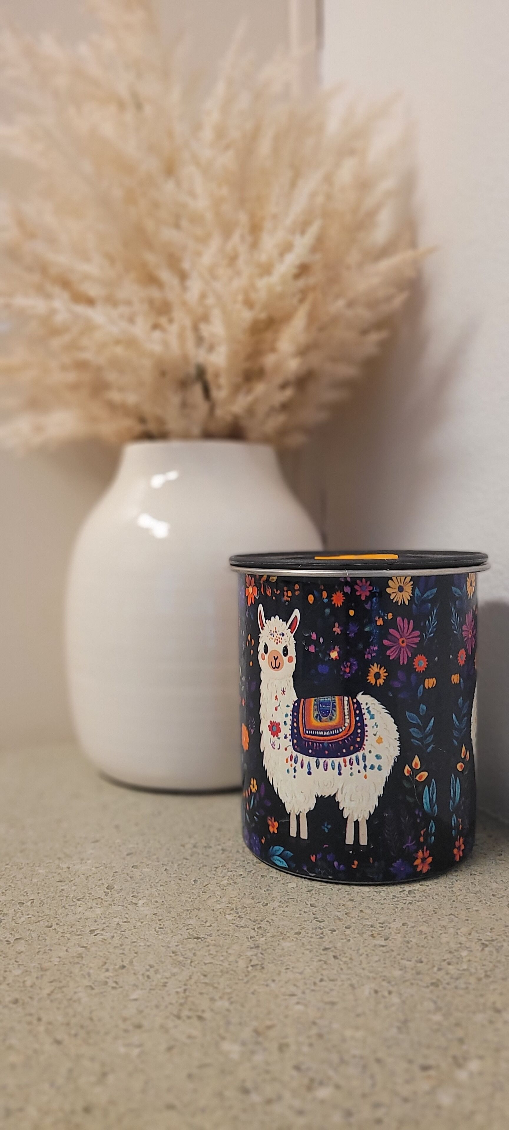 En dekorativ kop med et design af en lama, placeret på en overflade med struktur.