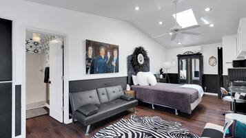 Un dormitorio moderno con cama, sofá, alfombra de cebra y ventilador de techo.