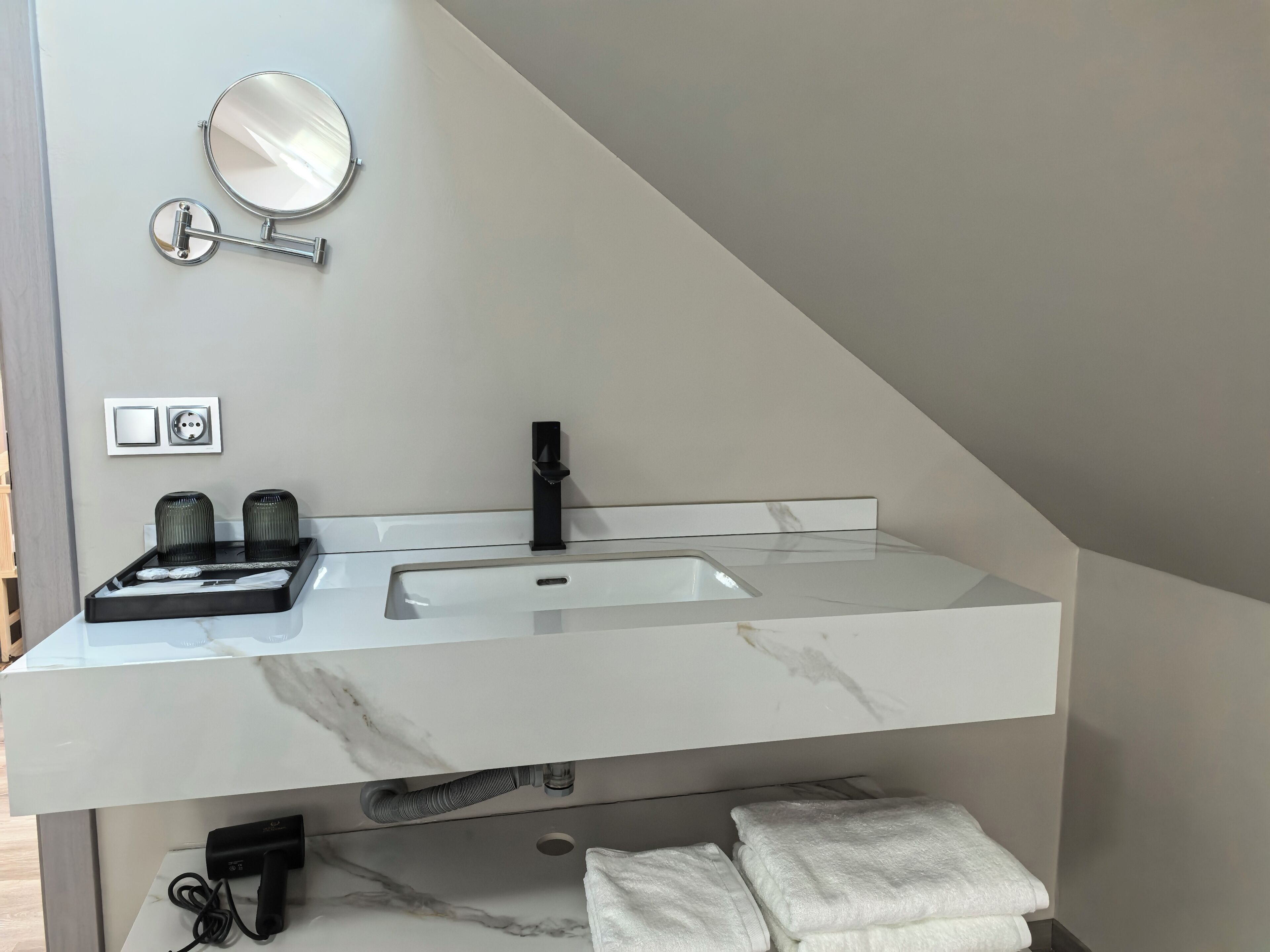 Un baño moderno con encimera de mármol blanco, grifo negro, espejo redondo y toallero.