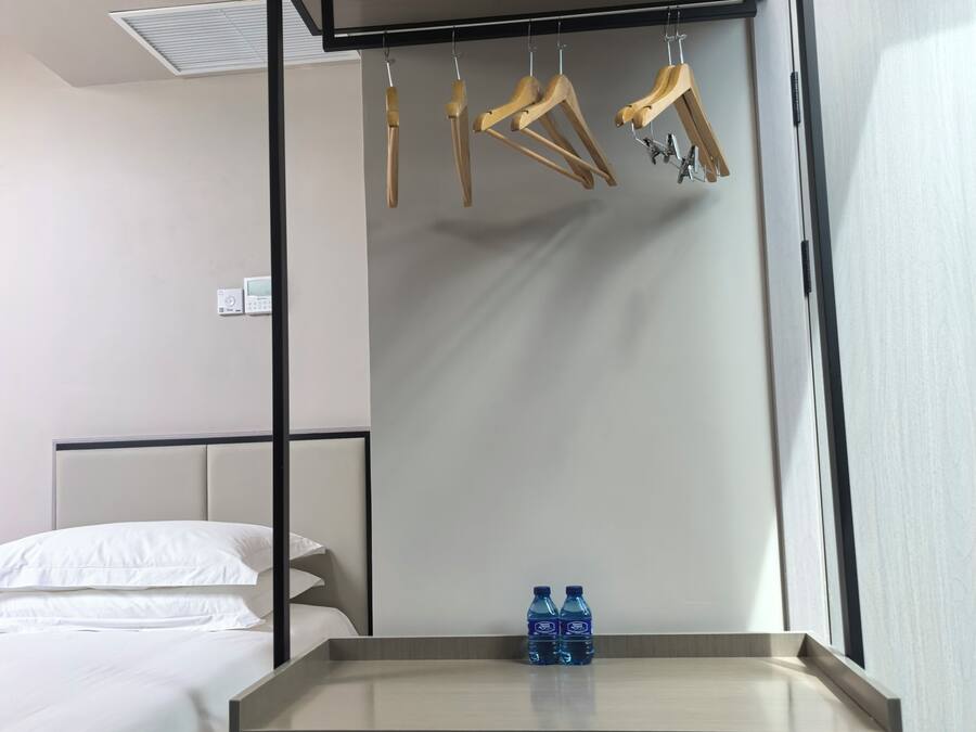 Ein Hotelzimmer mit einem Bett, einem Nachttisch mit zwei Wasserflaschen, einer Garderobe und einem Wandthermostat.