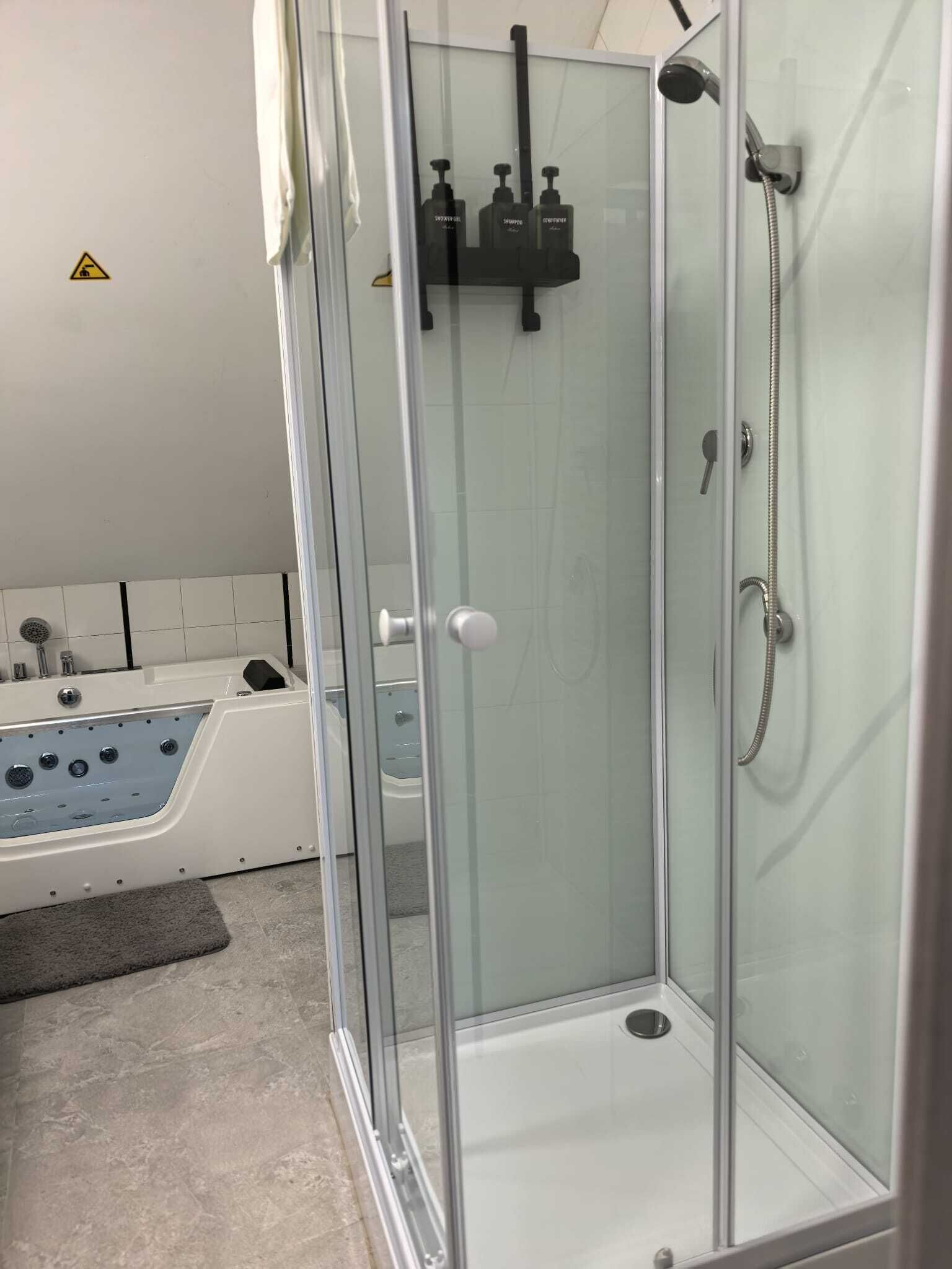 A glass-enclosed shower stall with a handheld showerhead and a handheld soap dispenser.