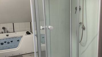A glass-enclosed shower stall with a handheld showerhead and a handheld soap dispenser.