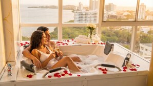 Ein Paar in einer Badewanne, umgeben von Rosenblättern, einem Blumenstrauß und Handtüchern.