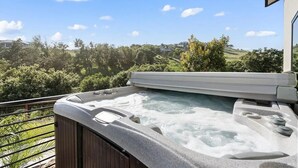 A hot tub on a balcony with a view of a green landscape and hills.