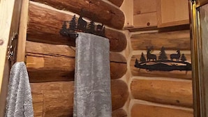 A log cabin interior with a wooden wall, a towel hanging on the wall, and a small shelf with decorative items. - Walden Cabin Yellowstone (Silver Gate)