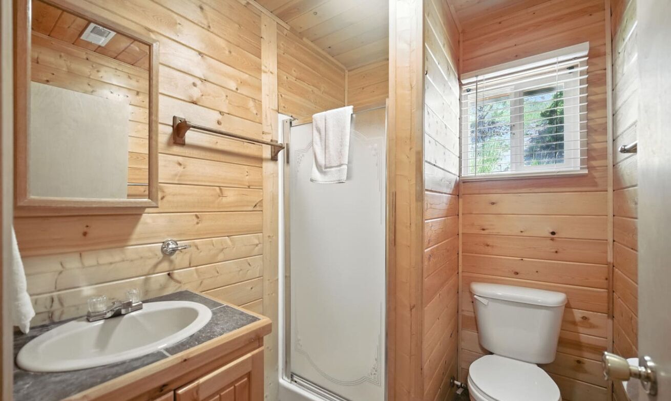 A wooden cabin bathroom with a sink, mirror, shower, and toilet.