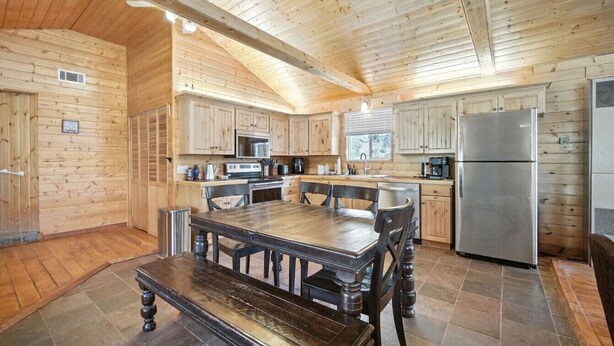 A wooden cabin with a kitchen featuring a large table, chairs, a refrigerator, and wooden cabinets. - Stunning Log Cabin Close to Panguitch Lake (Panguitch)