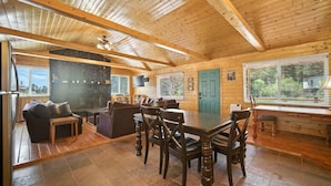 A spacious cabin interior with a wooden dining area, a stone fireplace, and large windows offering views of the outdoors. - Stunning Log Cabin Close to Panguitch Lake (Panguitch)