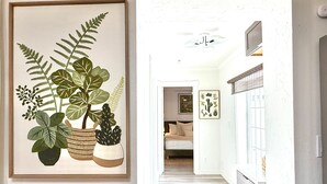 A hallway with a framed botanical print, a ceiling fan, and a bed in the background.
