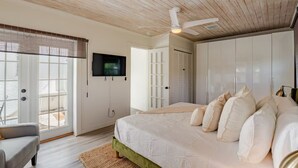 A bedroom with a bed, a TV, a ceiling fan, and a view of the outdoors.