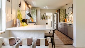A modern kitchen with a central island, white cabinetry, and a dining area with white chairs.