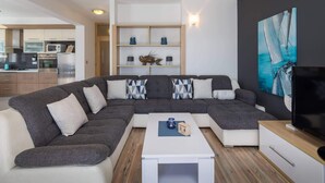 Un salon moderne avec un canapé d’angle, une table basse, un téléviseur et un tableau accroché au mur.